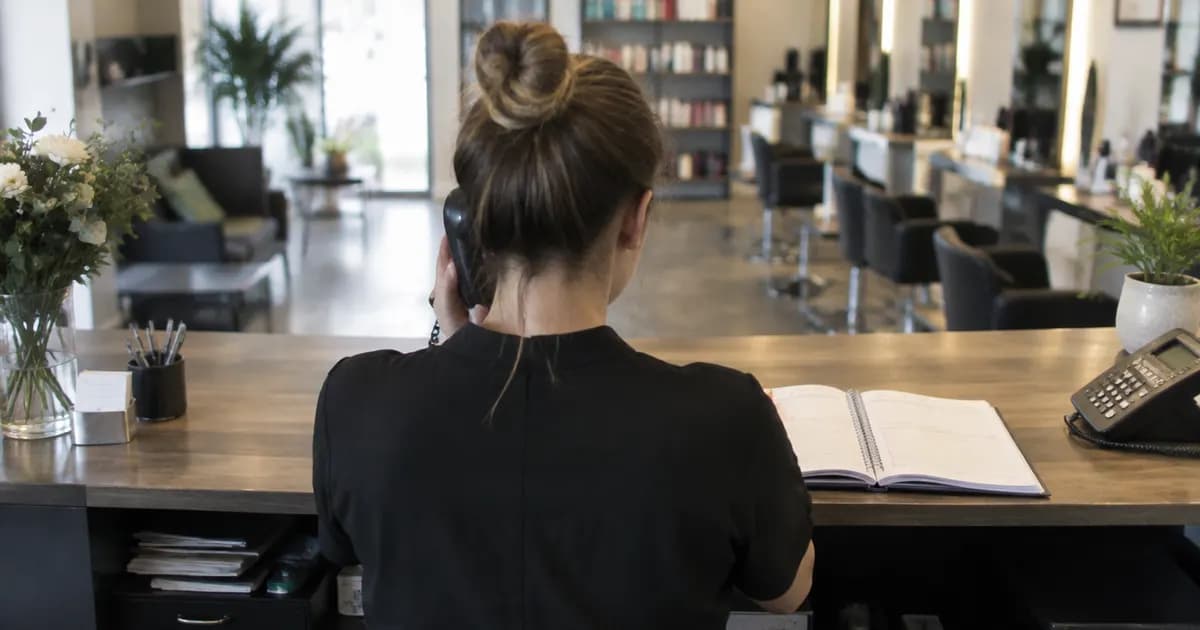 A salon receptionist taking a phone call at the front desk with an appointment book open